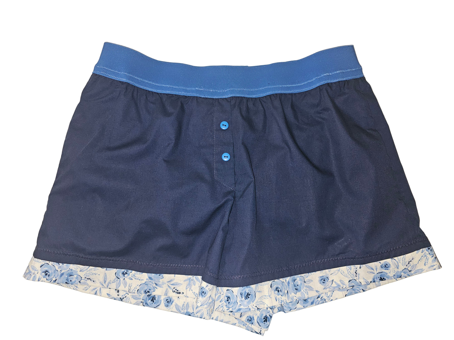 Medium women’s loungewear boxer shorts in deep midnight blue with a 2-inch elastic waistband in a lighter blue shade, finished with soft blue floral trim at the leg opening. Handmade cotton design with deep side pockets for comfortable, stylish lounging.