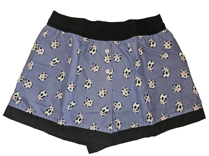 Women’s loungewear boxers in ‘Moo Mood Lounge’ print, featuring adorable black-and-white cows on a periwinkle background, black waistband and hem, soft breathable fabric, deep side pockets, and a handmade cozy fit.