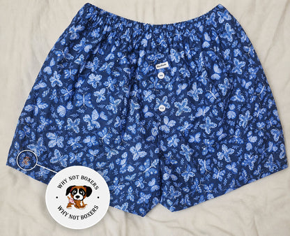 Women’s Medium boxer shorts with side pockets, featuring a deep blue base with a light blue butterfly print, elastic waistband, and front button detail, displayed on a light background; includes a zoomed inset highlighting the “Why Not Boxers” dog logo printed on the fabric.