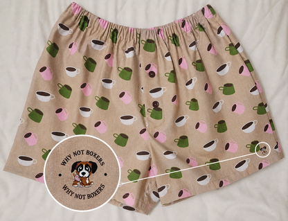 Women’s Medium boxer shorts with side pockets, featuring a warm beige base with a multicolor coffee cup print (green, pink, white, and brown), elastic waistband, and front button detail, displayed on a light background; includes a zoomed inset highlighting the “Why Not Boxers” dog logo printed on the fabric.