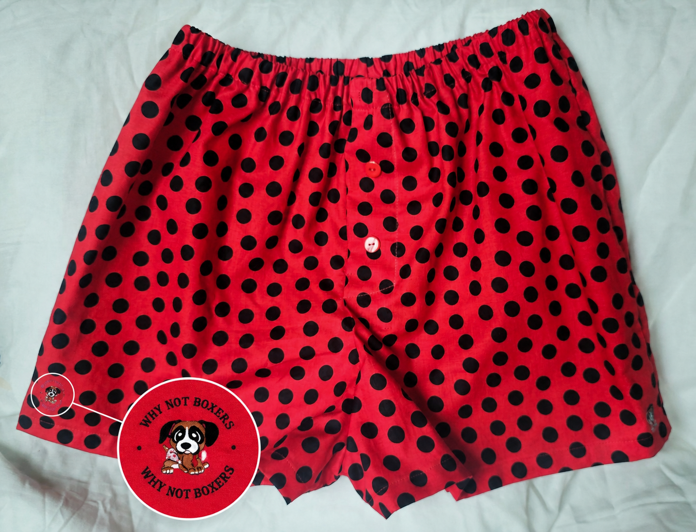 Red women’s boxer shorts in size Medium with side pockets, featuring black polka dots, an elastic waistband, and a front button detail, displayed on a light background; includes a small inset highlighting the “Why Not Boxers” dog logo printed on the fabric.