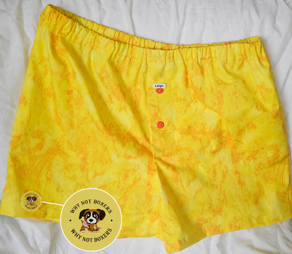 Women’s Medium boxer shorts with side pockets, featuring a bright yellow base with subtle orange textured patterning, elastic waistband, and front button detail, displayed on a light background; includes a zoomed inset highlighting the “Why Not Boxers” dog logo printed on the fabric.Medium