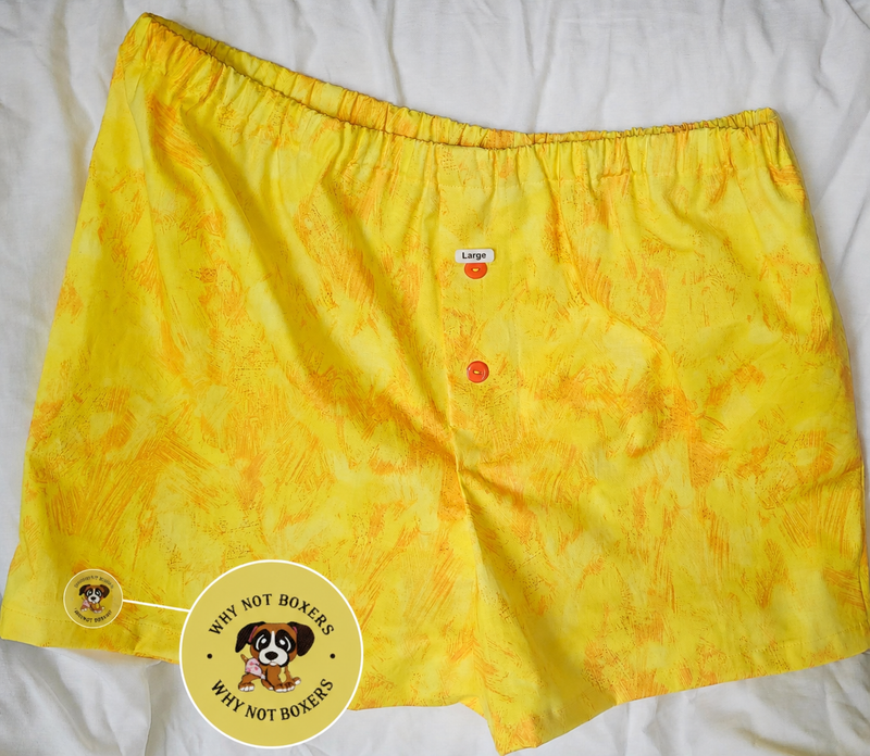 Women’s Medium boxer shorts with side pockets, featuring a bright yellow base with subtle orange textured patterning, elastic waistband, and front button detail, displayed on a light background; includes a zoomed inset highlighting the “Why Not Boxers” dog logo printed on the fabric.Medium